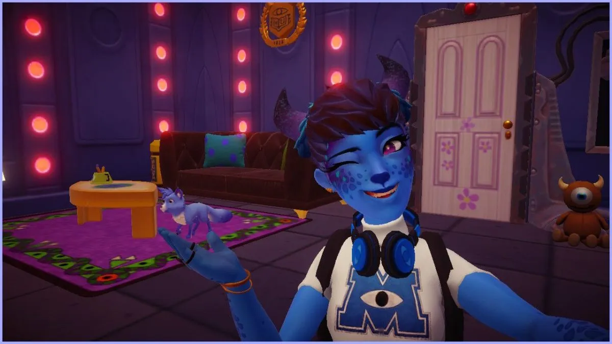 A fem-presenting Disney Dreamlight Valley avatar with blue skin and horns gestures towards a blue fox roaming in the ground. The avatar is winking and wearing a Monster's University shirt in white with a blue logo, and blue headphones around their neck. In the background, the wallpaper has glowing red lights, Boo's door from Monster's Inc. can be seen on the right, and there's a brown couch by the wall with a purple rug nearby.