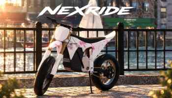 NexRide official artwork showing a white electric dirt bike with pink floral details parked beside a waterfront, with the NexRide logo above.